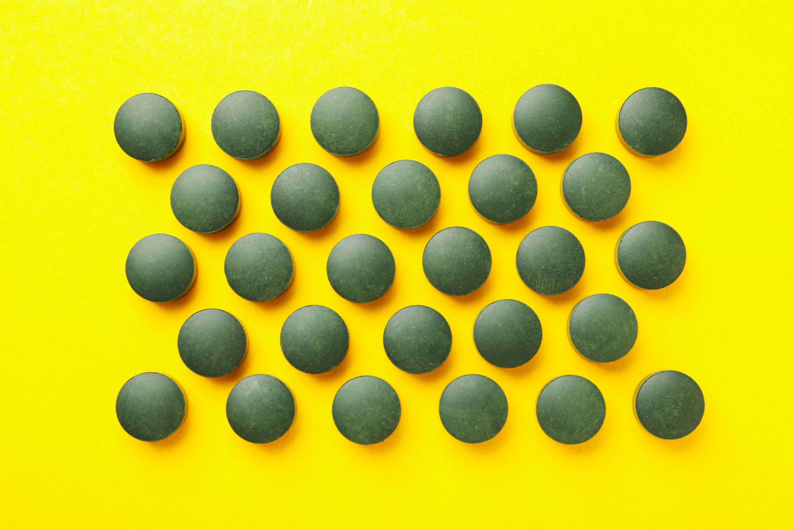Flat lay with spirulina pills on yellow background, top view